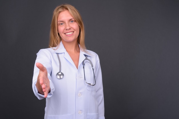 Hermosa joven médico con cabello rubio contra la pared gris