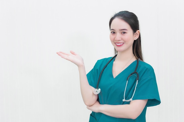 Hermosa joven médico de la mujer asiática en un uniforme verde está parado y sonríe mientras apunta a la parte superior