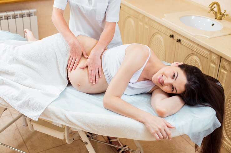 Hermosa joven médico terapeuta de masaje en una sala de cosmetología haciendo un masaje a una niña embarazada con cabello largo