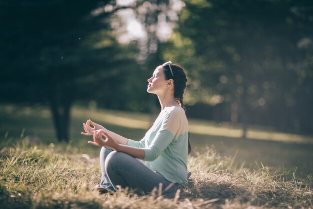 Hermosa joven meditando en posición de loto sentada en el césped. foto con espacio de copia