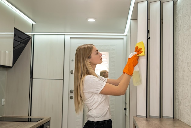 Hermosa joven en mitones naranjas haciendo limpieza en la cocina Concepto de limpieza