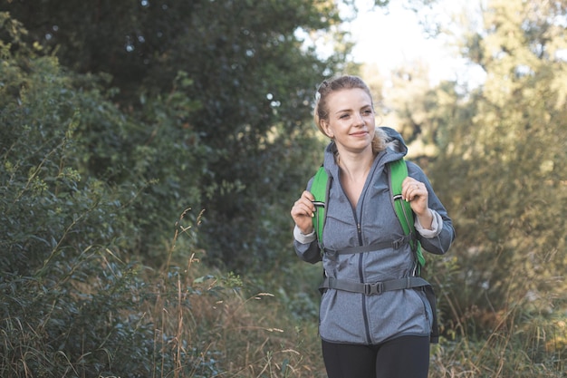 La hermosa joven con mochila está caminando en el bosque