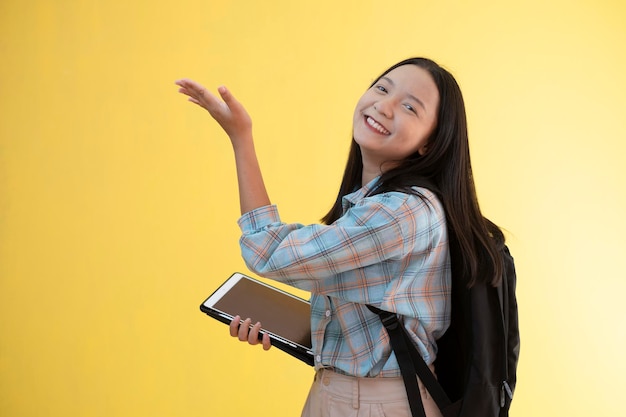 Hermosa joven con mochila y portátil con fondo amarillo.