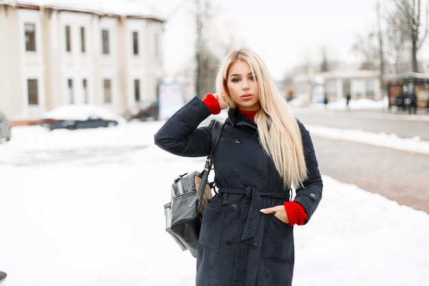 Hermosa joven de moda en un elegante abrigo con una bolsa caminando en la ciudad