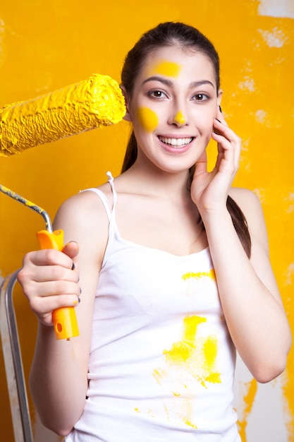 Hermosa joven modelo caucásica en pantalones cortos de colores y camisa blanca y posando sosteniendo un estabilizador en sus manos, pintando la pared y mirando a cámara. Tiro del estudio.