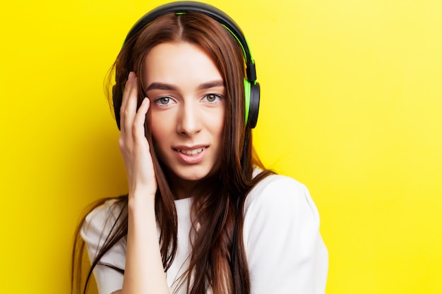 Hermosa joven modelo escucha música en auriculares en amarillo