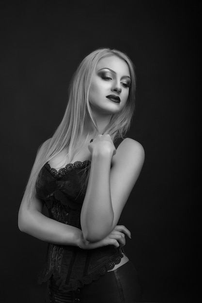 Hermosa joven modelo con maquillaje brillante y cabello largo y rubio lleva corsé con encaje. Foto de estudio en blanco y negro