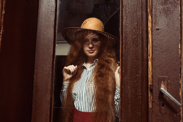 Hermosa joven modelo pelirroja con sombrero de paja con sombra en el rostro y pecas