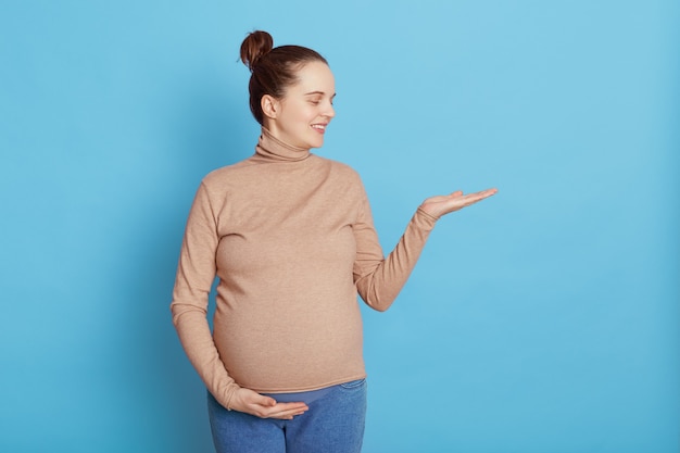 Hermosa joven con moño esperando bebé posando aislado en azul