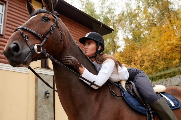 Hermosa joven montando a caballo al aire libre Concepto de cuidado de animales Descanso rural y ocio Idea de turismo verde Joven europea con casco y uniforme