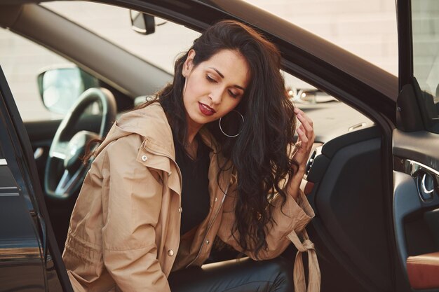 Hermosa joven morena con cabello rizado sentada dentro de un auto moderno