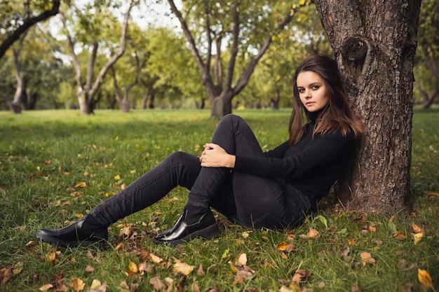 Una hermosa joven morena camina por el parque de otoño con un suéter negro y un abrigo. Idea y concepto de expectativa