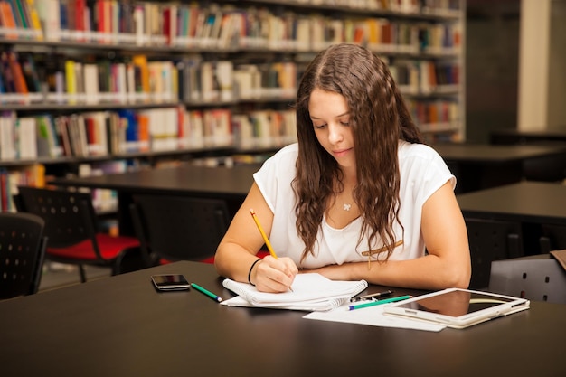 Foto hermosa joven morena haciendo algunos deberes sola en la biblioteca
