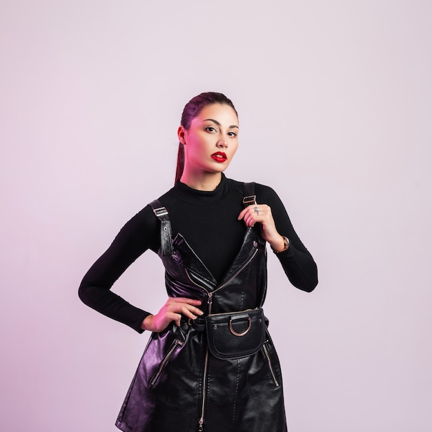 Hermosa joven morena con peinado de moda en camisa vintage en vestido sexy negro de moda de cuero posando en el estudio. Chica atractiva con hermosos labios rojos en el interior. Ropa para mujeres.