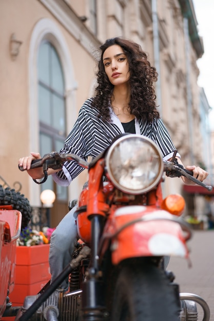 Hermosa joven morena con pelo rizado sentado en una motocicleta roja