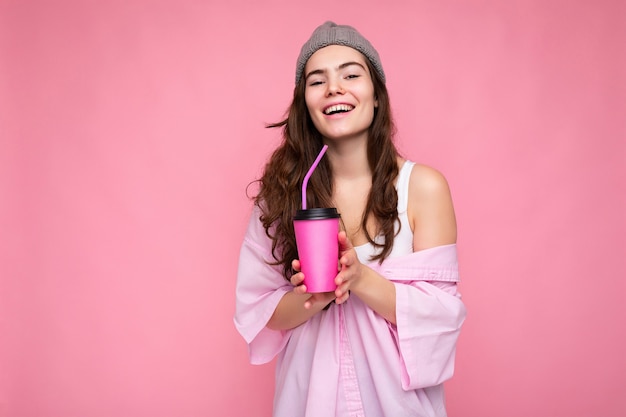 Hermosa joven morena positiva vistiendo ropa casual elegante aislada sobre pared de colores de fondo sosteniendo una taza de papel para maqueta tomando café mirando a la cámara.