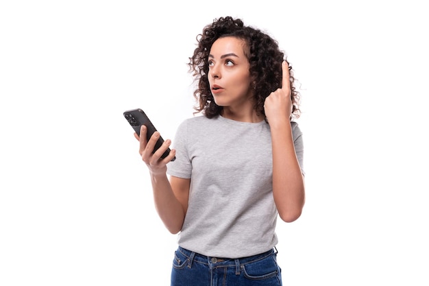 Una hermosa joven morena rizada con una camiseta gris usa un concepto de estilo de vida de la gente de un teléfono inteligente