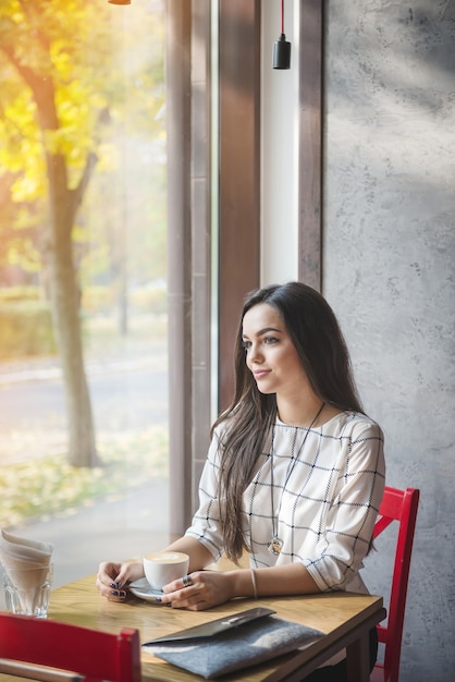 Hermosa joven morena sentada en un café y bebiendo té.