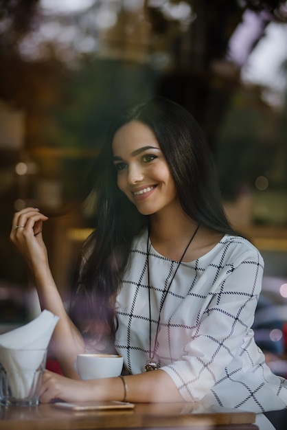 Hermosa joven morena sentada en un café y bebiendo té.