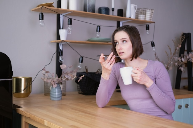 Hermosa joven morena sonriente a mujer en ropa casual con una taza de té mediante teléfono móvil