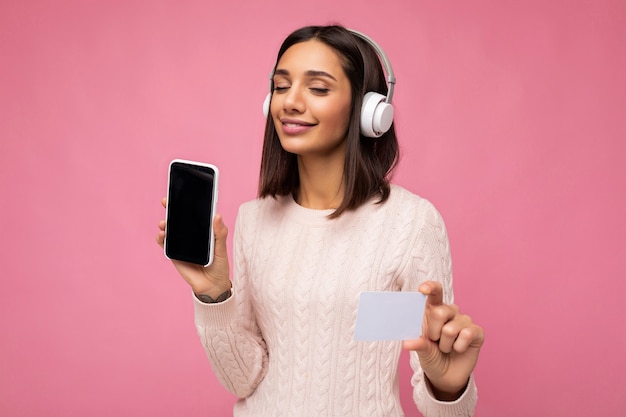 Hermosa joven morena vestida con un suéter casual rosa aislado sobre una pared de fondo rosa