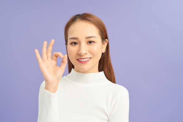 Hermosa joven mostrando el signo de OK contra la pared violeta