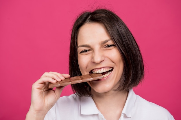 Hermosa joven muerde una barra de chocolate