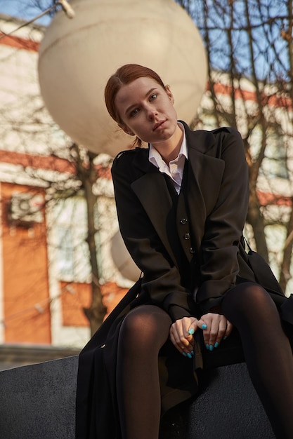 Hermosa joven mujer caucásica en abrigo con pelo largo sentado al aire libre en el parque