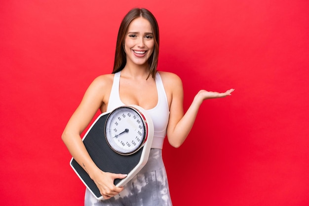 Hermosa joven mujer caucásica aislada sobre fondo rojo con máquina de pesaje