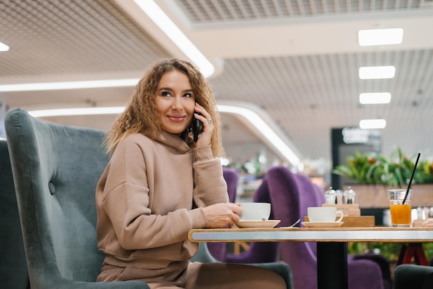 Hermosa joven mujer caucásica hablando por teléfono inteligente en la cafetería