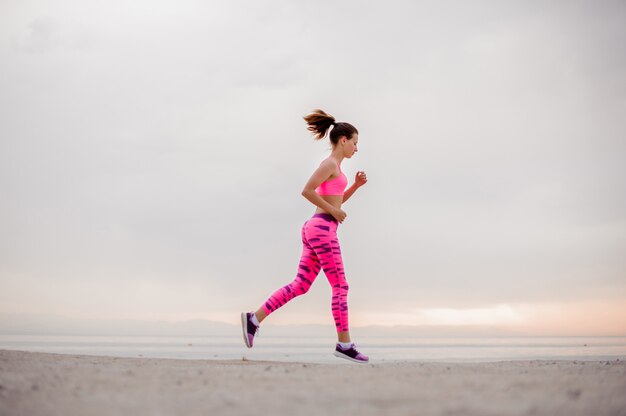 Hermosa y joven mujer corriendo por la orilla del mar en la mañana