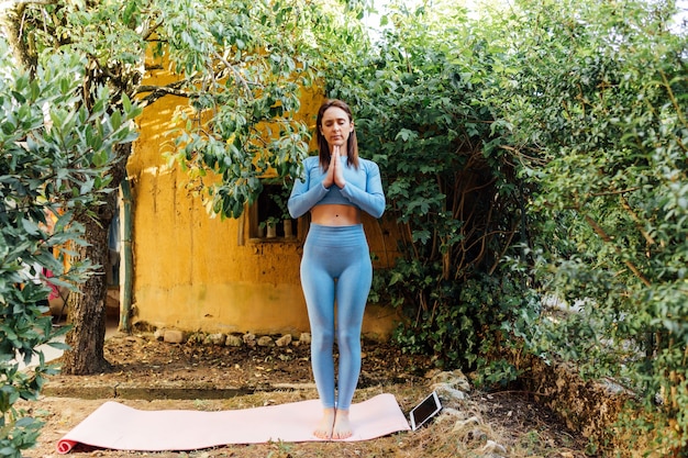 Hermosa joven mujer de mediana edad haciendo yoga en el jardín de su casa con tableta. Concepto de vida sana, meditación