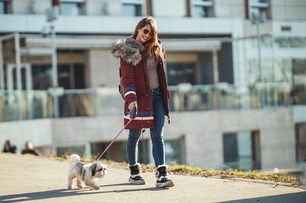 Hermosa joven mujer de moda está pasando tiempo con su lindo perro mascota, caminando por la calle de la ciudad.