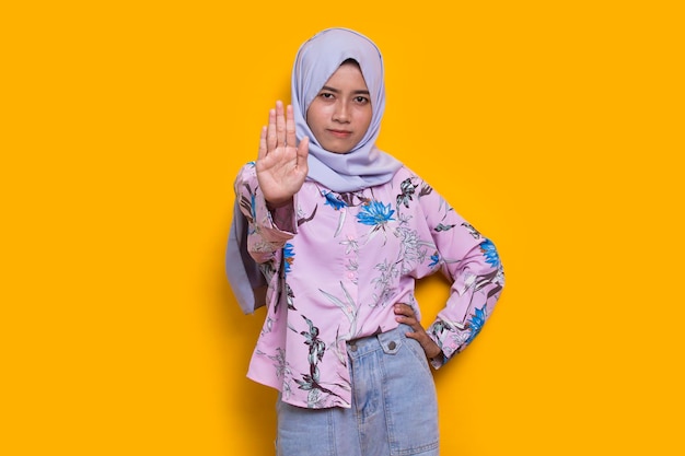 hermosa joven mujer musulmana mano haciendo señal de stop con expresión seria gesto de defensa en amarillo