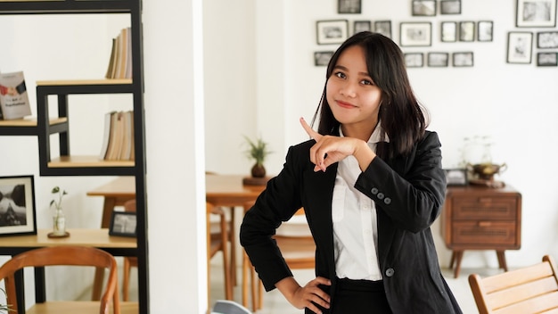 Hermosa joven mujer de negocios asiática en traje y señalando con el dedo las manos en la oficina