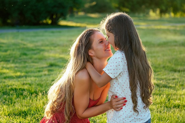 Hermosa y joven mujer de pelo largo jugando con su hija abrazar y acariciar en un día de verano en el parque. maternidad feliz y un maravilloso concepto de infancia