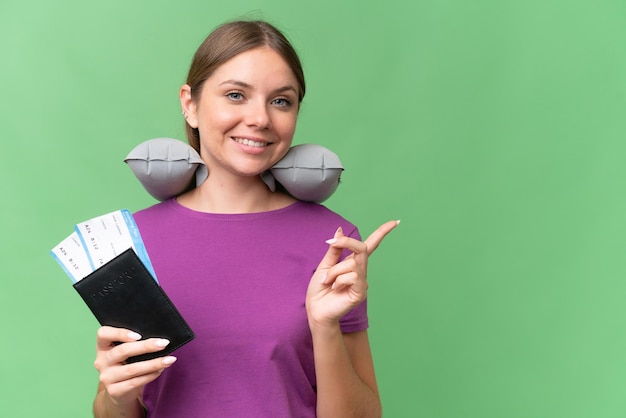 Hermosa joven mujer rubia con almohada de viaje inflable sobre fondo aislado apuntando hacia un lado para presentar un producto