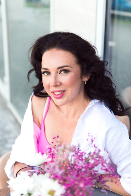 Hermosa joven mujer sonriente sentada en el café de la calle con decoración de flores