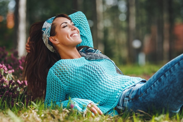 Hermosa joven mujer sonriente tumbada en la hierba florida y disfrutando del soleado día de primavera.