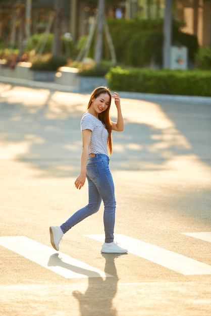 Hermosa joven mujer vietnamita sonriente tocando su cabello al cruzar la calle