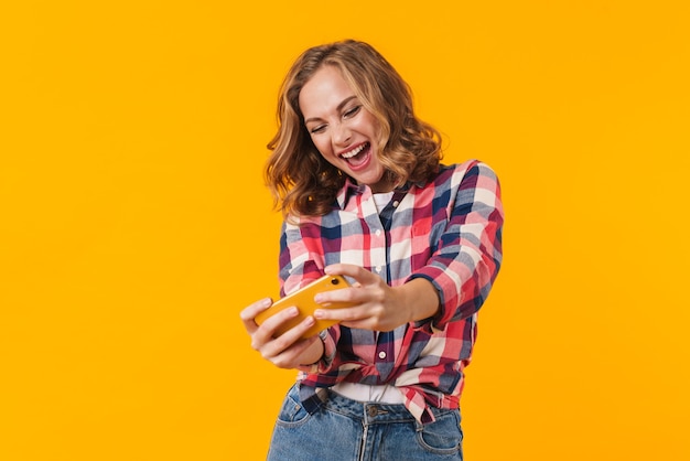 Hermosa joven mujer vistiendo camisa a cuadros sonriendo y sosteniendo teléfono celular aislado