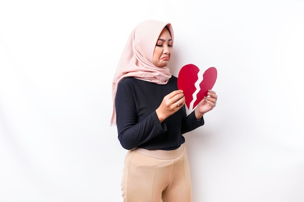 Hermosa joven musulmana asiática expresó su tristeza mientras sostenía el corazón roto aislado de fondo blanco