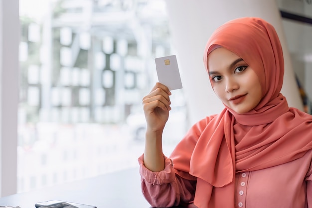 Hermosa joven musulmana asiática mujer de negocios en hijab rosa y ropa casual manos mostrando una tarjeta de crédito blanca