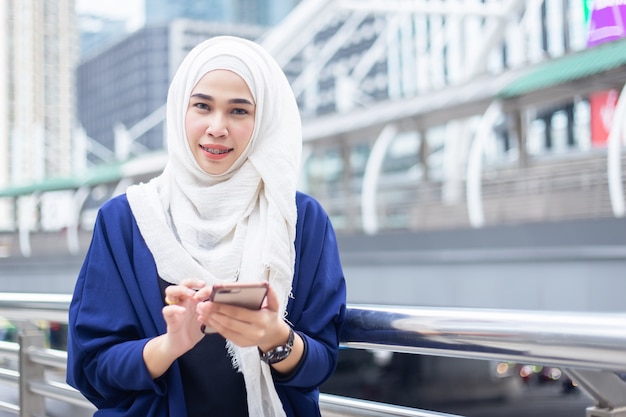 Hermosa joven musulmana asiática de negocios en un traje con pañuelo en la cabeza (hijab) uesing smartphone