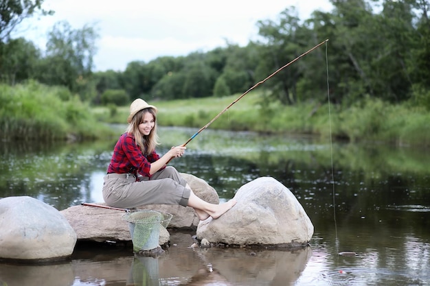 Hermosa joven en la naturaleza junto al río con una caña de pescar