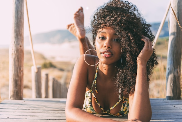 Hermosa joven negra acostada en un puente peatonal de madera en la playa