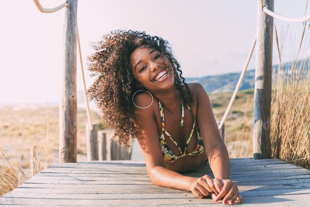 Hermosa joven negra acostada en un puente peatonal de madera en la playa