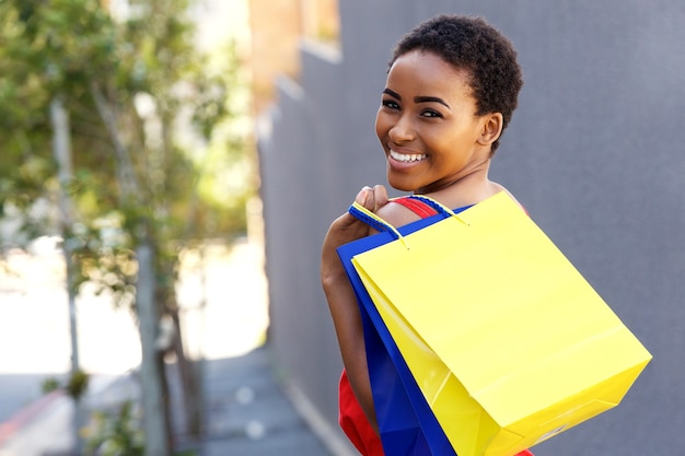 Hermosa joven negra sonriendo con bolsas de compras afuera