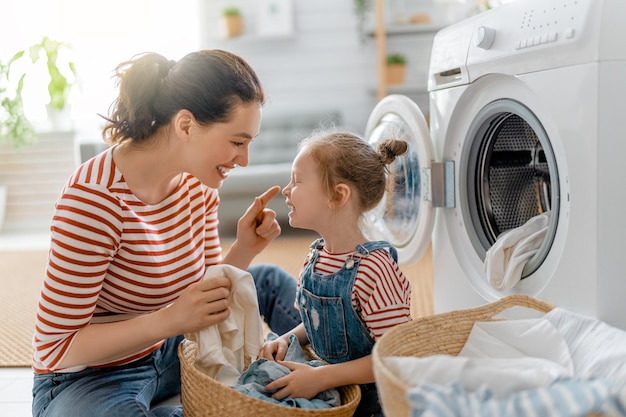 Hermosa joven y niña pequeña ayudante están sonriendo mientras lava la ropa en casa