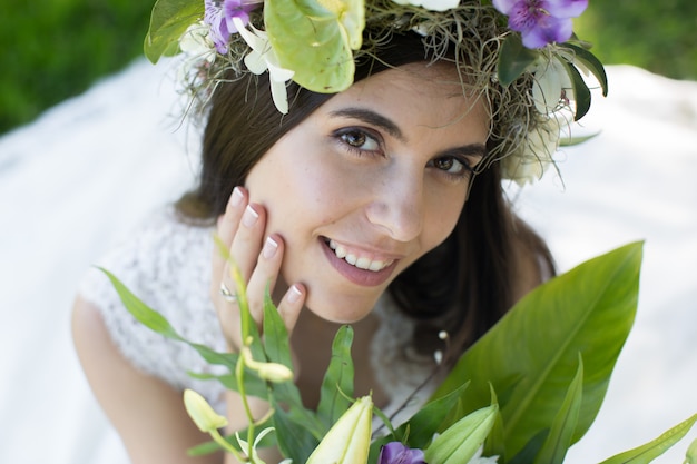 Hermosa joven novia en una corona de flores con un ramo de flores en la mano